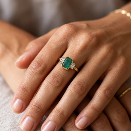 Anillo de oro con esmeralda rectangular y diamantes baguette puesto en la mano